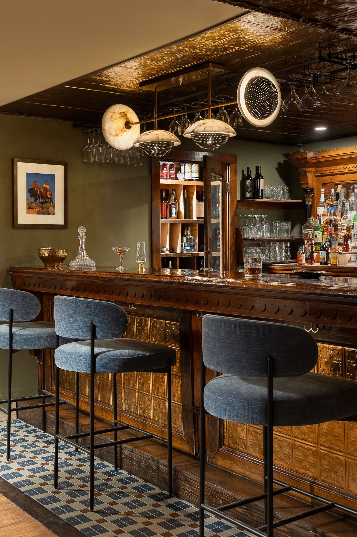 Uma área de bar com banquetas, balcão e diversas garrafas e copos.