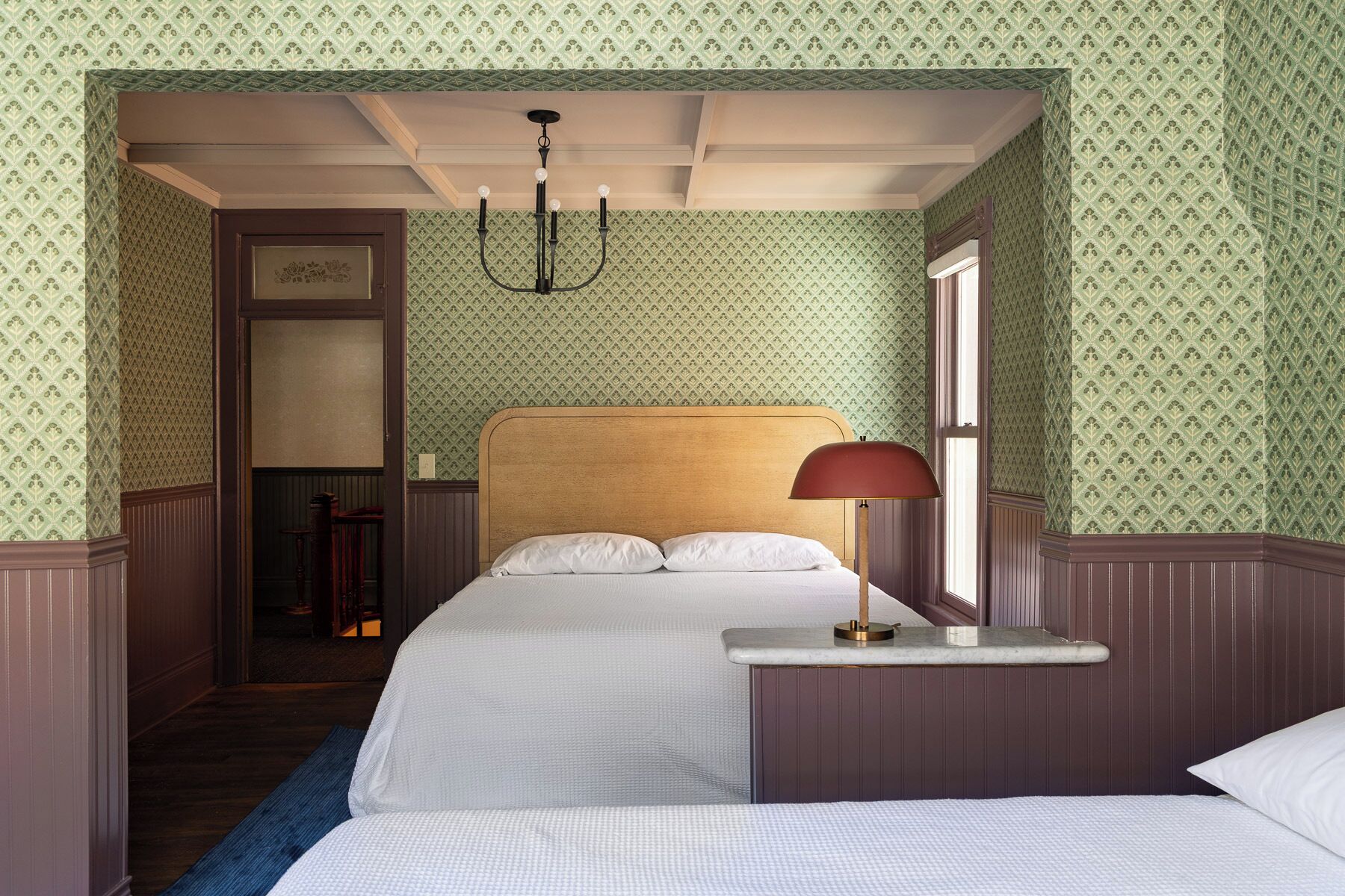 Habitación de hotel con dos camas, un candelabro, una mesita de noche y un ventanal.