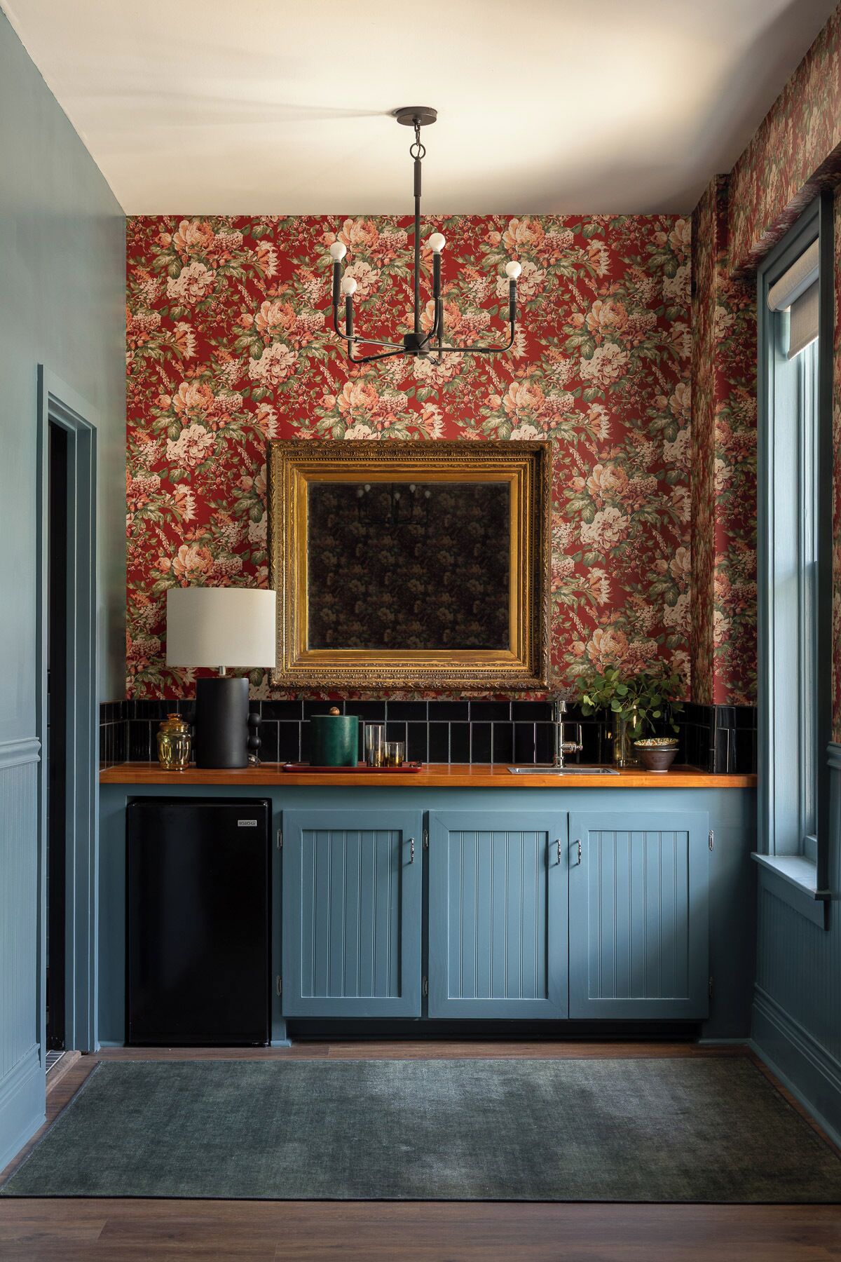 Una cocina con papel tapiz floral, un candelabro, un cuadro enmarcado y un refrigerador pequeño.