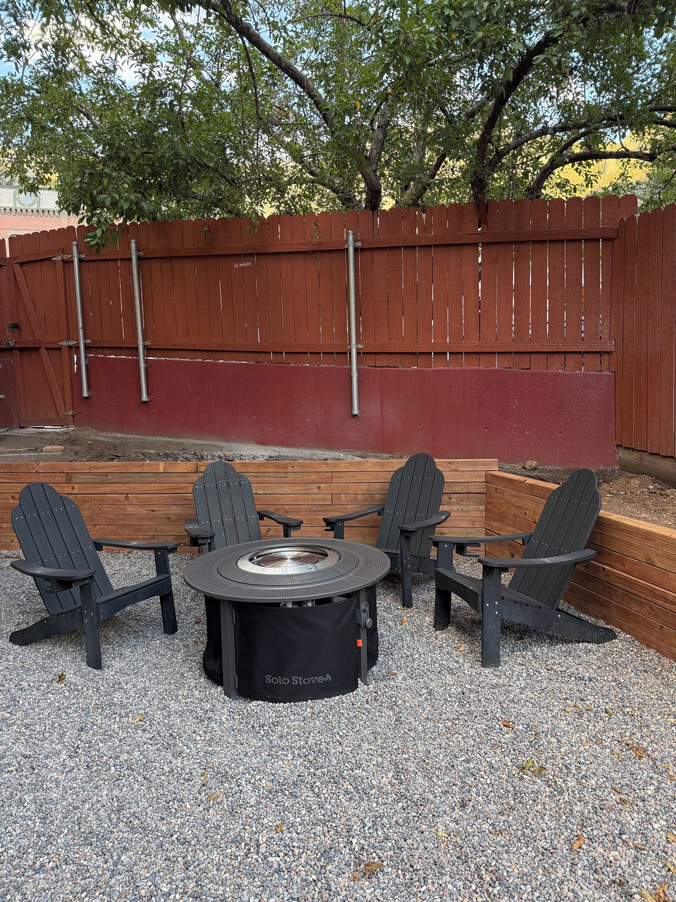 Een terras met Adirondack-stoelen en een ronde tafel met een ingebouwde kookplaat.