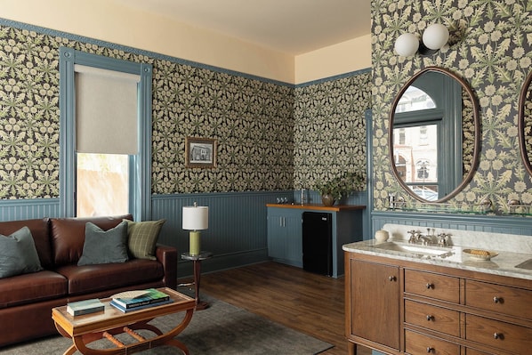 A room with a brown leather sofa, a wooden coffee table with books, a blue cabinet with a marble countertop, and a patterned wallpaper. - St. Elmo Hotel (Ouray)