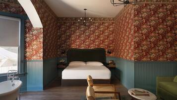 A bedroom with a large bed, a vintage bathtub, and a green armchair.