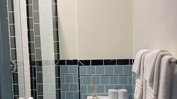 Un baño con inodoro, cubo de basura, ducha y toallero.