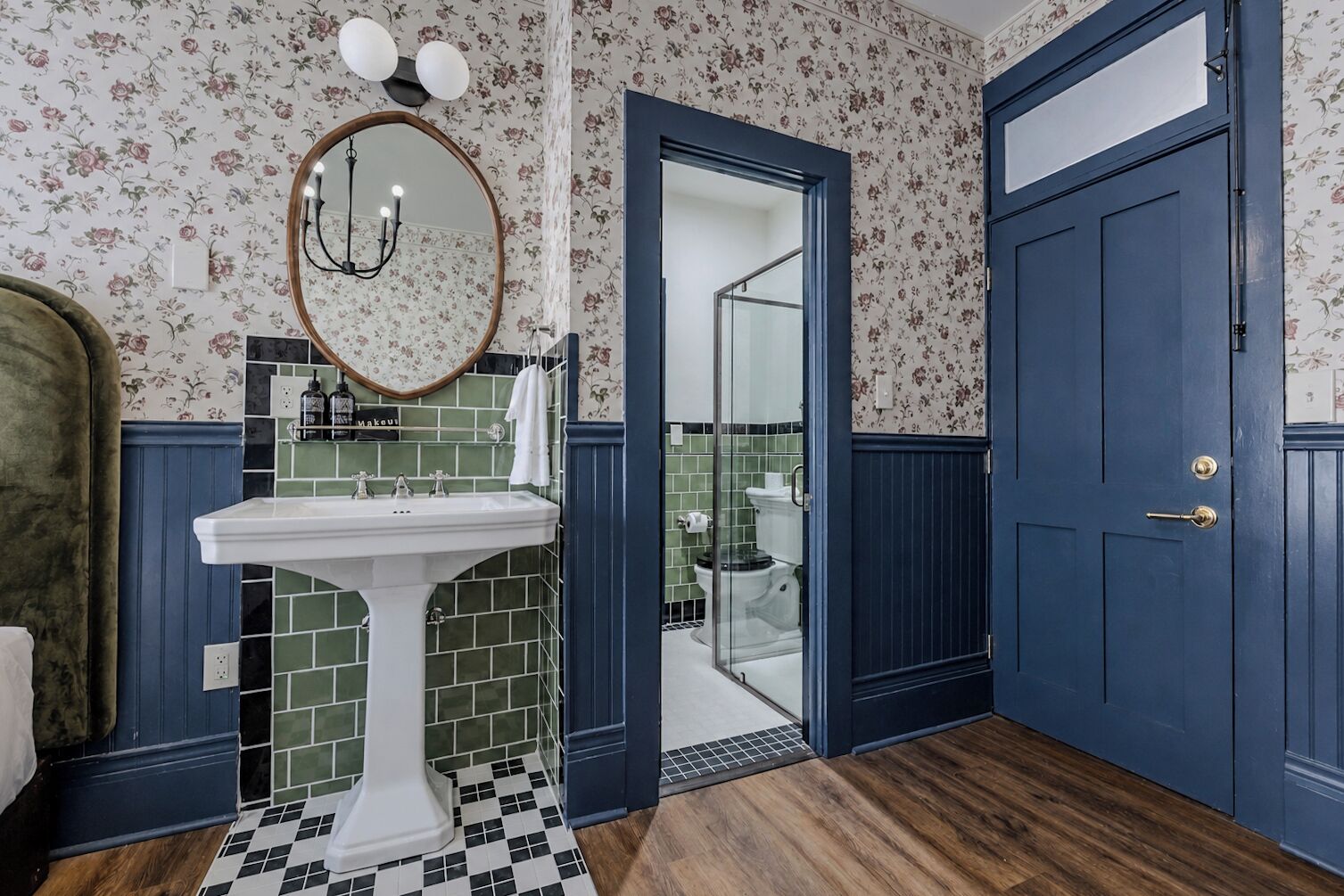 A bathroom with a white pedestal sink, a mirror with a wooden frame, and a blue door.