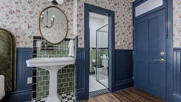 A bathroom with a white pedestal sink, a mirror with a wooden frame, and a blue door.