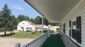A covered porch with a green floor, white railings, and hanging flower baskets.