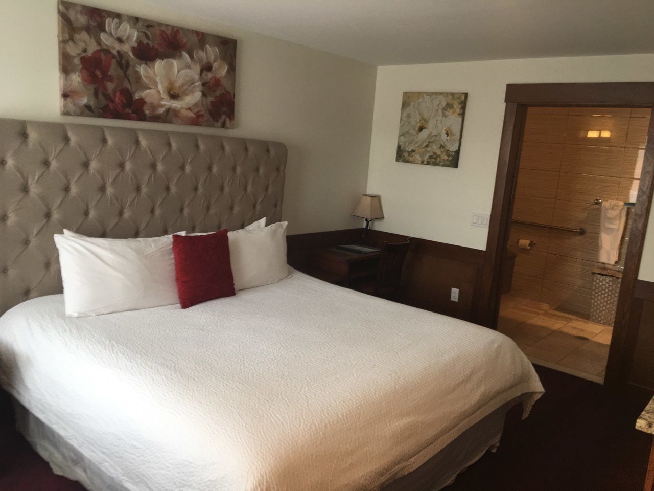 Ein Hotelzimmer mit einem großen Bett, einem gepolsterten Kopfteil, einem Nachttisch aus Holz, einer Lampe und einem Duschbereich.