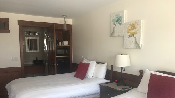 A hotel room with two beds, a nightstand, a lamp, a clock, and a wardrobe with a mirror.