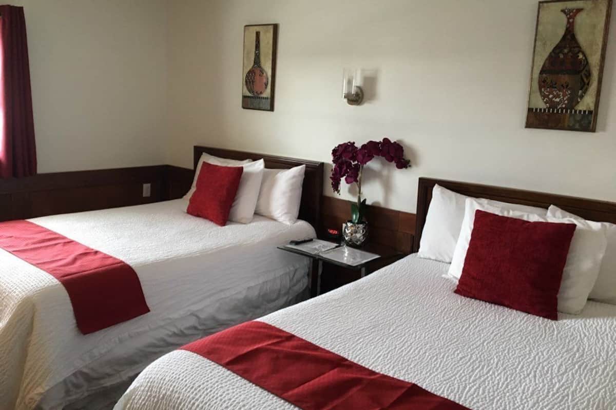 Une chambre d’hôtel avec deux lits, chacun agrémenté de draps blancs et de touches de couleur rouge, une table de chevet avec un vase de fleurs et des œuvres d’art accrochées aux murs.