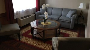A living room with a grey sofa, a round coffee table with a vase of flowers, a bench, and a lamp on a side table.