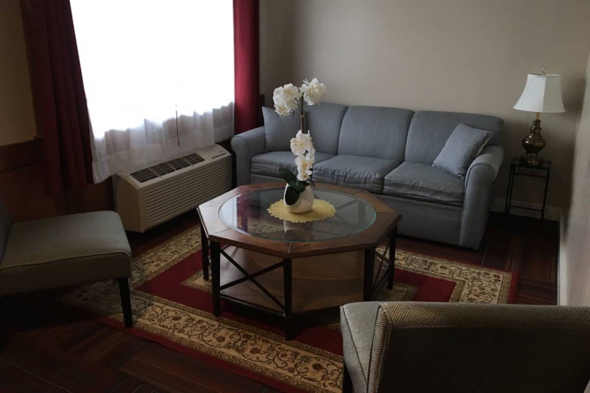 Un salon avec un canapé gris, une table basse ronde ornée d’un vase de fleurs, un banc et une lampe sur une table d’appoint.