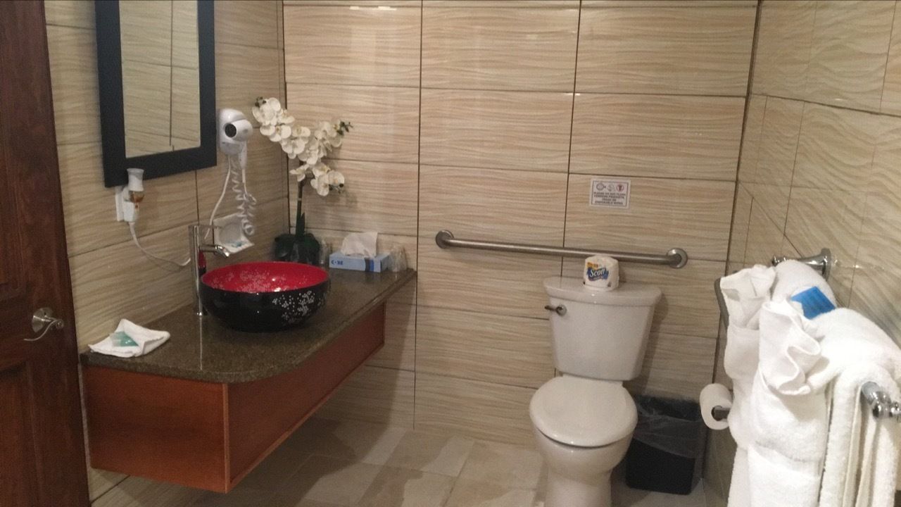 A bathroom with a marble wall, a sink with a red basin, a toilet, and a hand dryer.