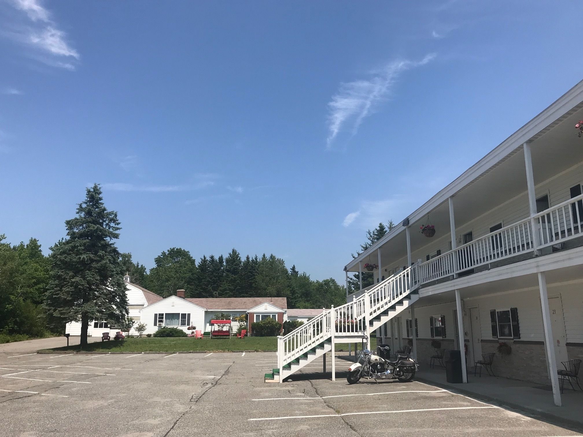 A motel with a covered parking area, a staircase leading to the upper floor, and a motorcycle parked in the lot.