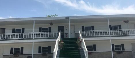 A two-story motel with a central staircase, a balcony on the upper floor, and a parking lot in front.
