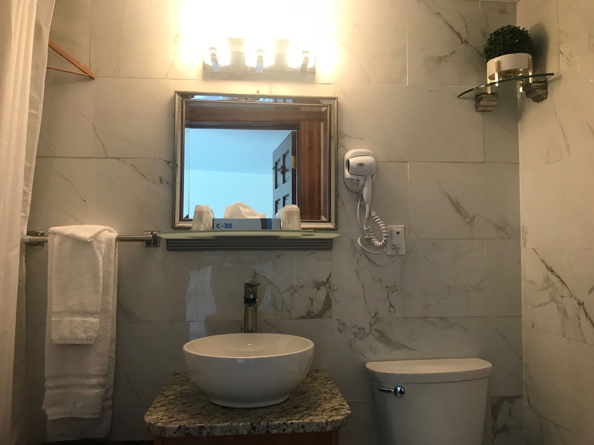 A bathroom with a marble sink, a toilet, a hairdryer, and a mirror with lights above it.