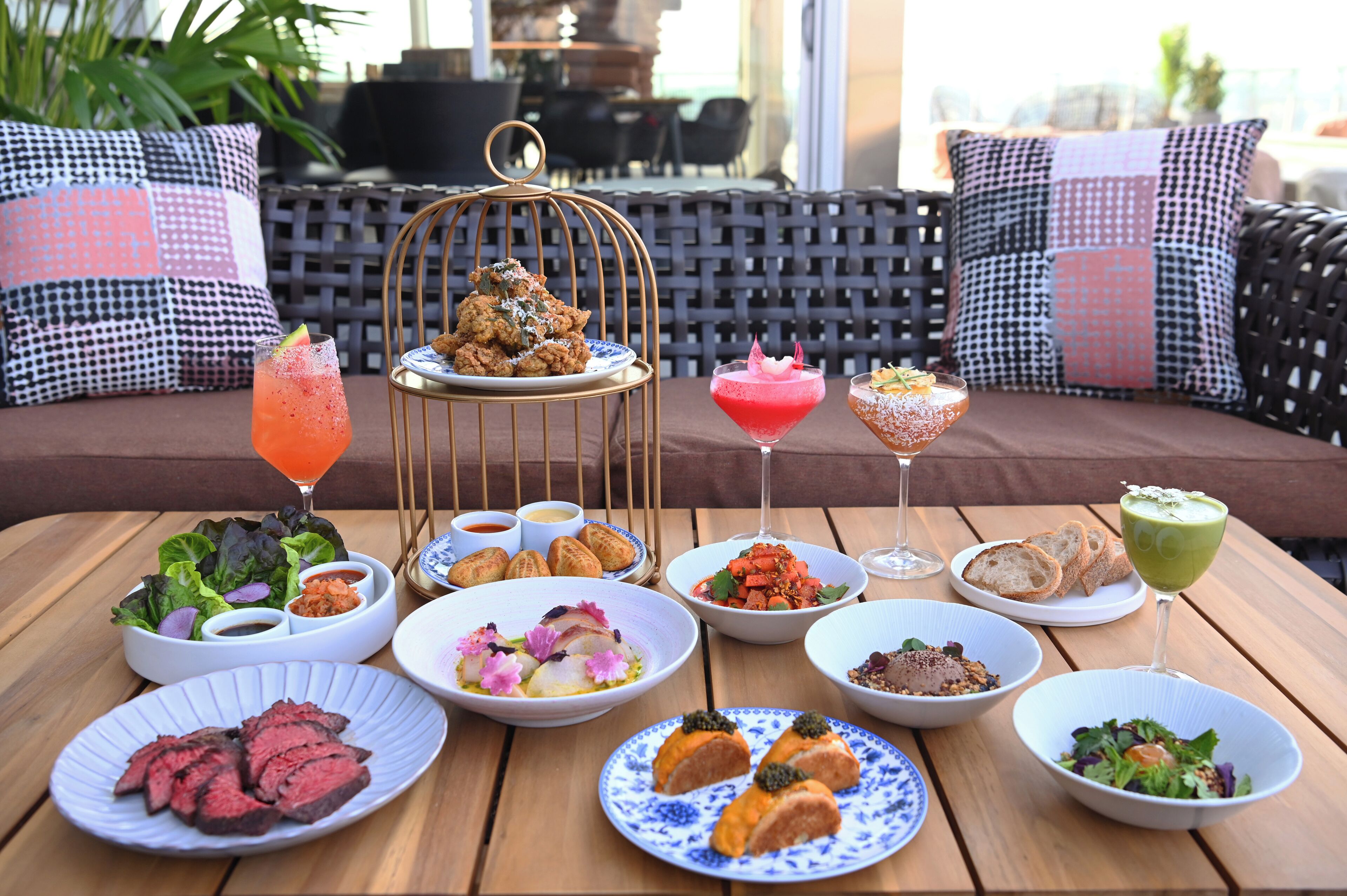 A table set with various dishes, drinks, and a decorative birdcage centerpiece.