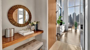A modern interior with a wooden vanity, a round mirror, and a view of a cityscape through large windows.