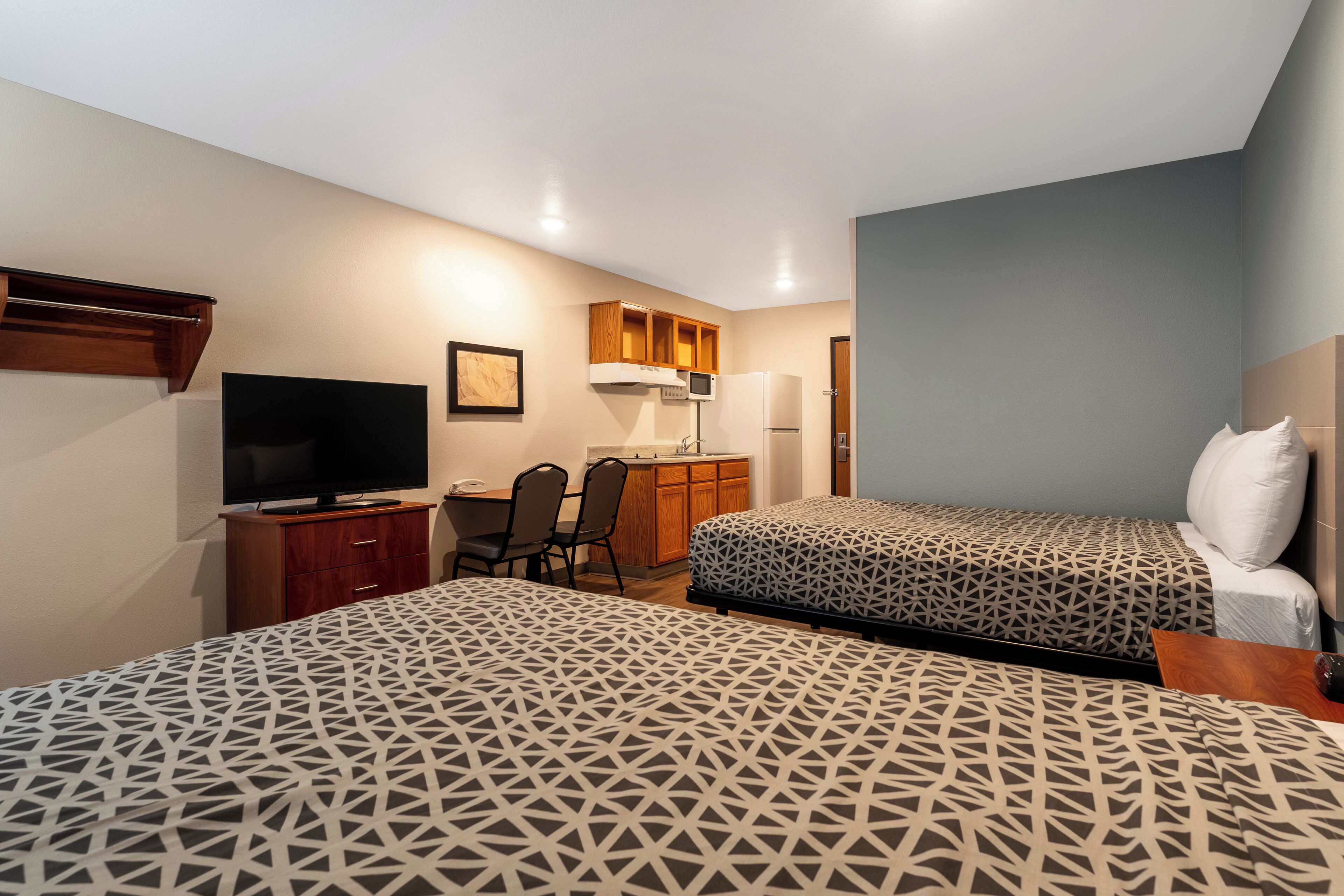 A hotel room with two beds, a desk, a television, and a kitchenette.