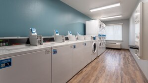 Una sala de bugaderia amb diverses rentadores i assecadores, una balança digital i un codi QR per servei autònom.