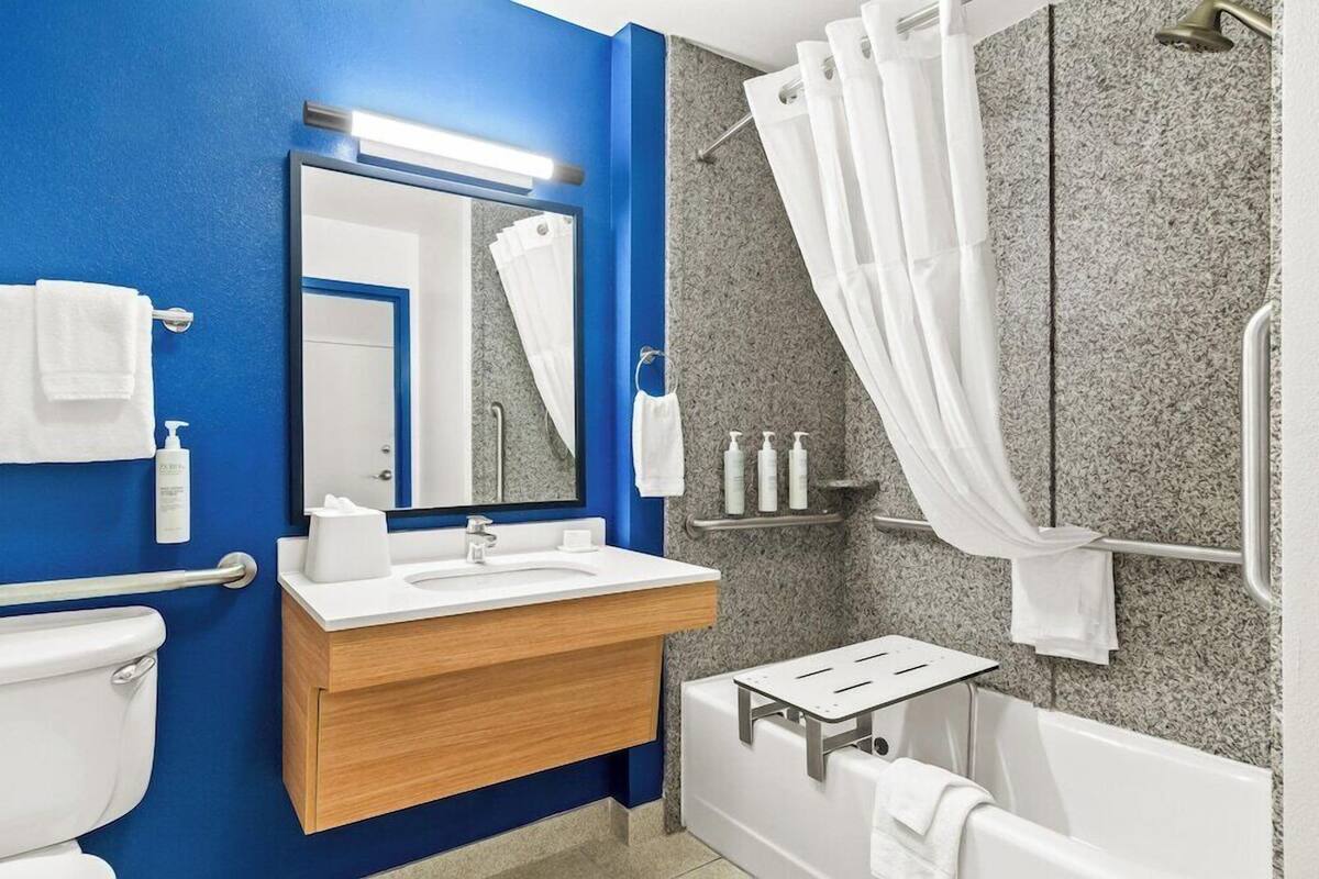 Ein Badezimmer mit blauer Wand, Waschbecken in Weiß, Spiegel, Dusche und Toilette.