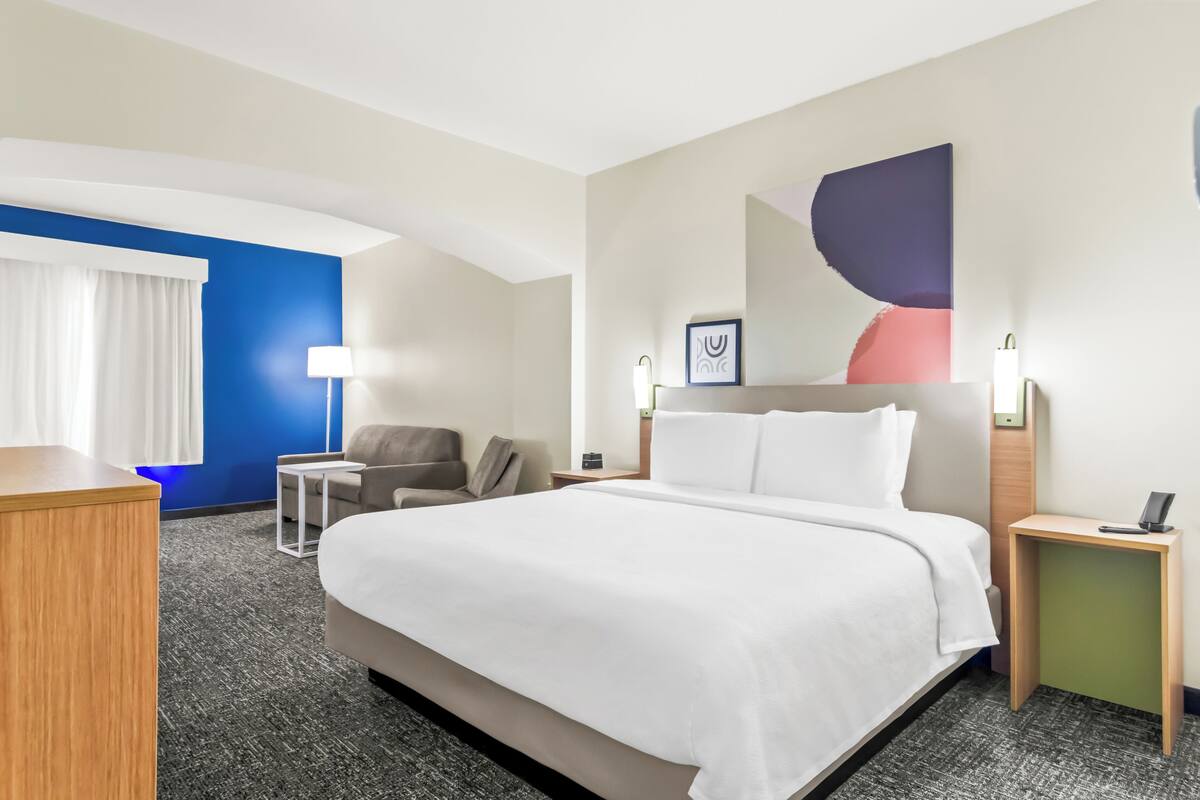 Ein Hotelzimmer mit einem großen Bett, einem Schreibtisch, einem Sessel, einem kleinen Tisch und einer Lampe.