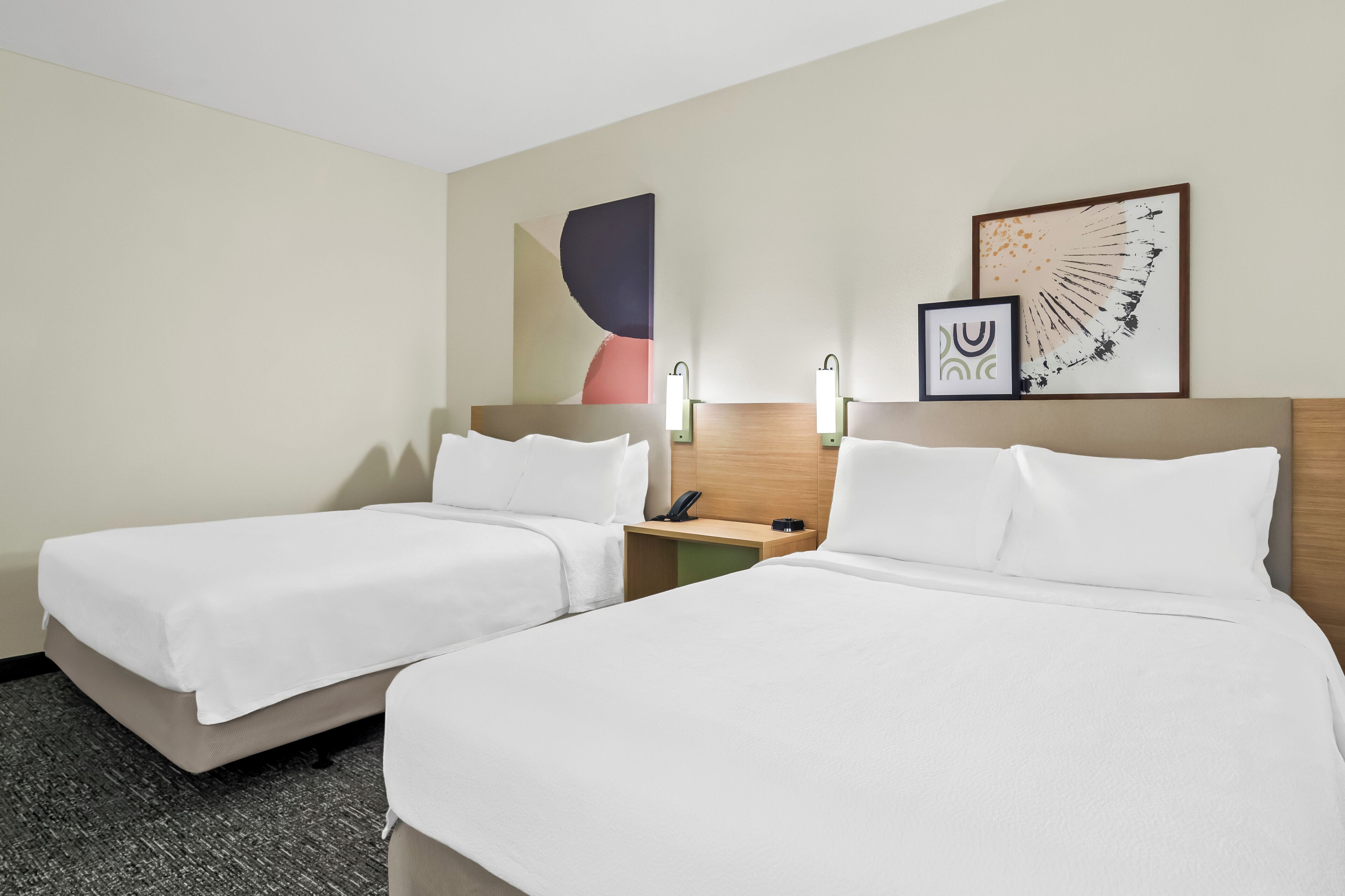 A hotel room with two beds, a nightstand, a phone, and two wall-mounted lamps.