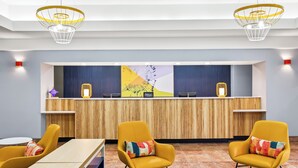 Um hall de hotel moderno com balcão de recepção, cadeiras amarelas e área de atendimento em madeira.