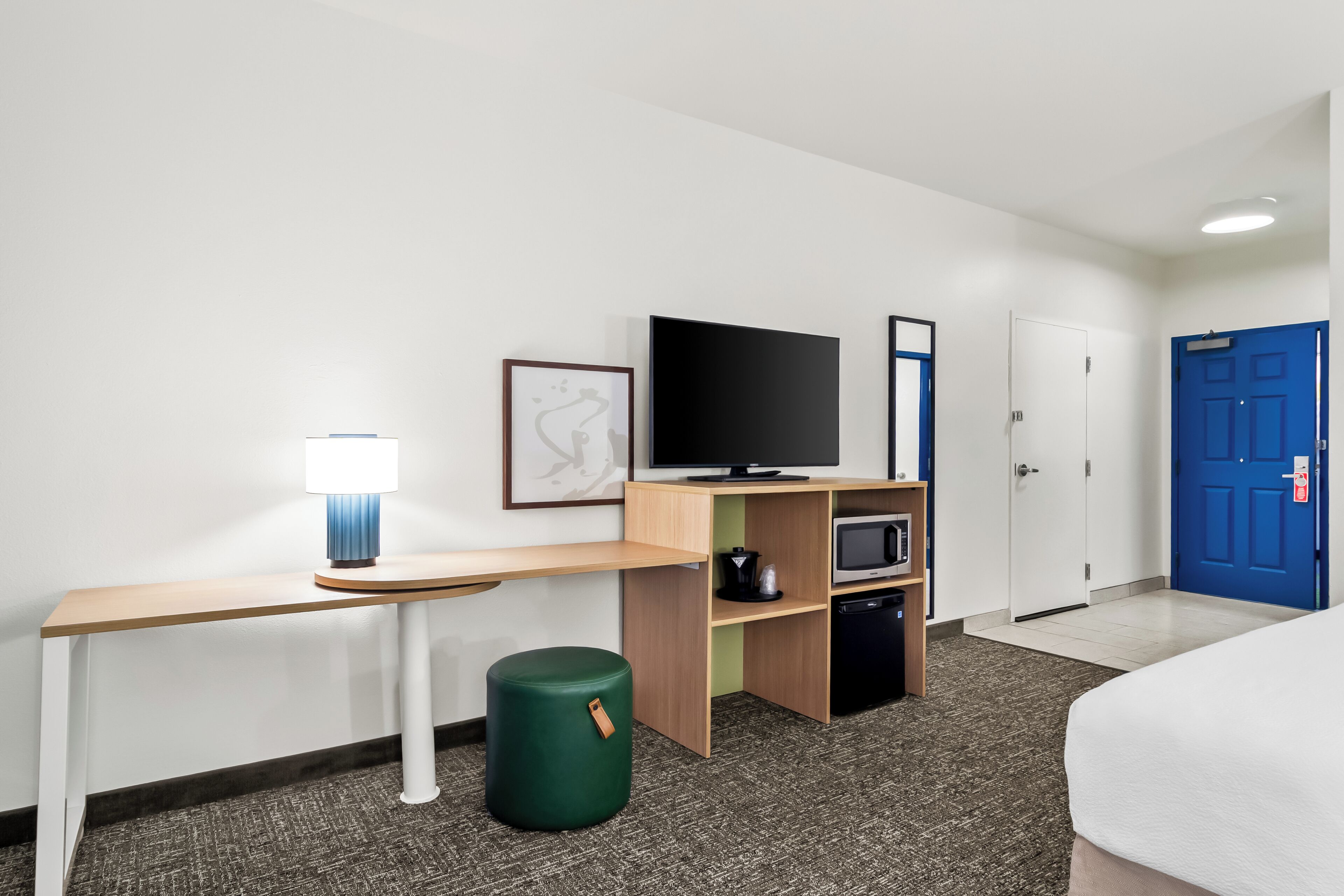 A hotel room with a bed, a desk with a lamp, a flat-screen TV, a microwave, and a small trash bin.