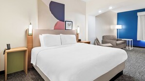 Quarto de hotel com uma cama grande, uma escrivaninha, uma cadeira e uma parede azul de destaque.
