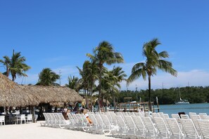 A beachside restaurant with outdoor seating and a thatched roof.