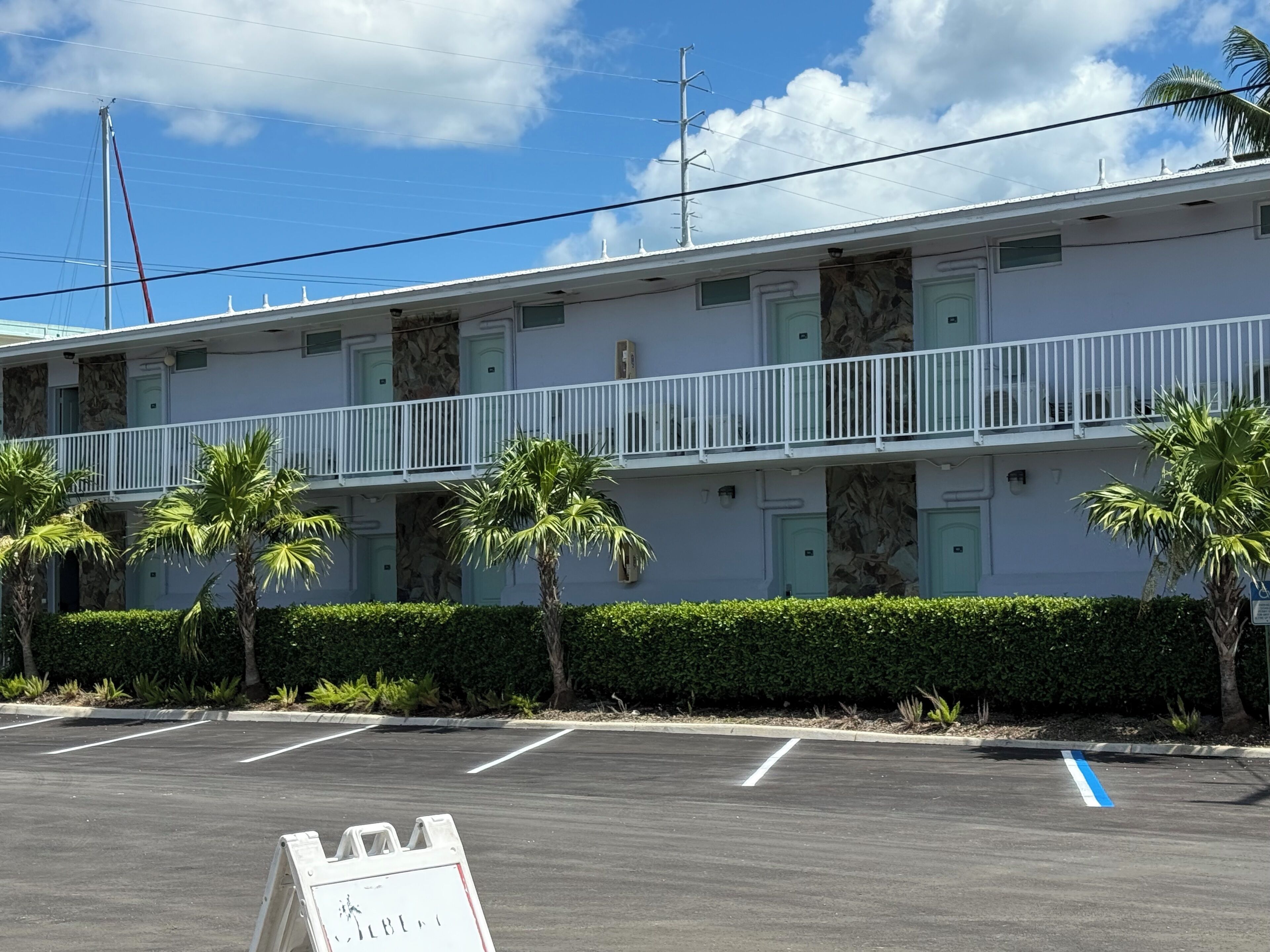A two-story motel with a white exterior, multiple balconies, and palm trees in the parking lot.