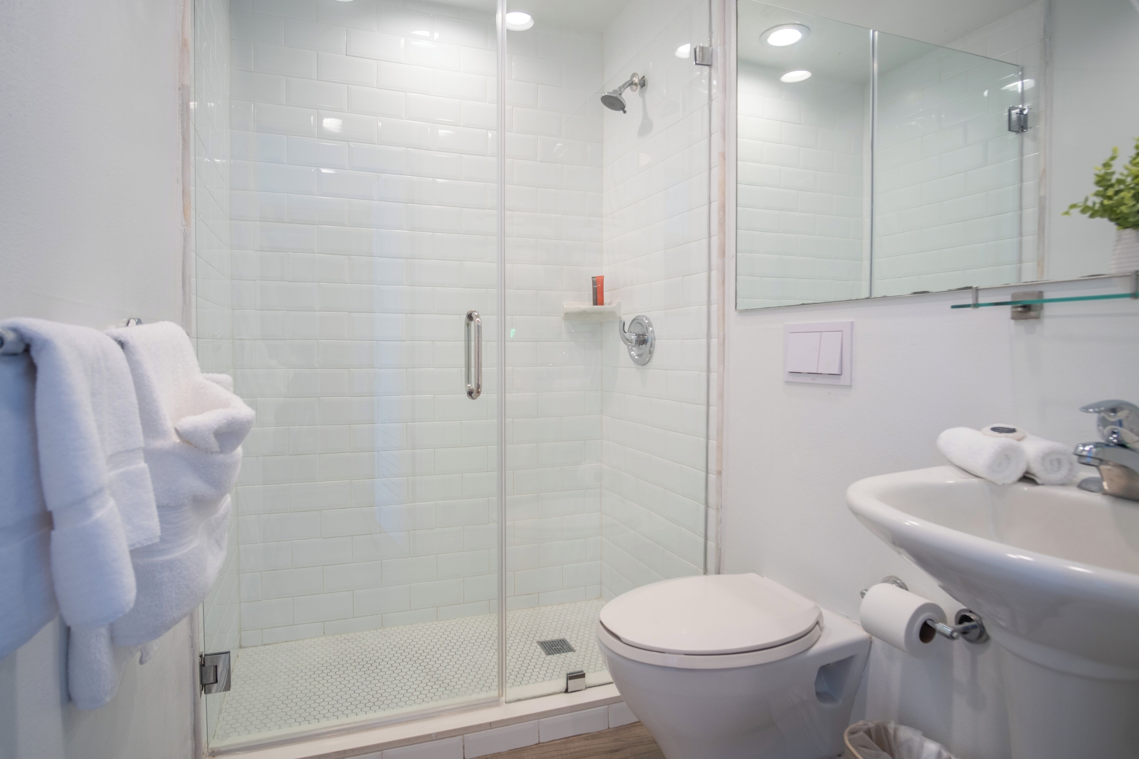 Un bagno moderno con doccia vetrata, un WC bianco e un lavandino con specchio sopra.