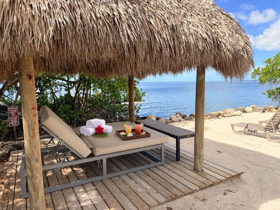 A beachside lounge with a thatched roof, a wooden deck, and a view of the ocean.