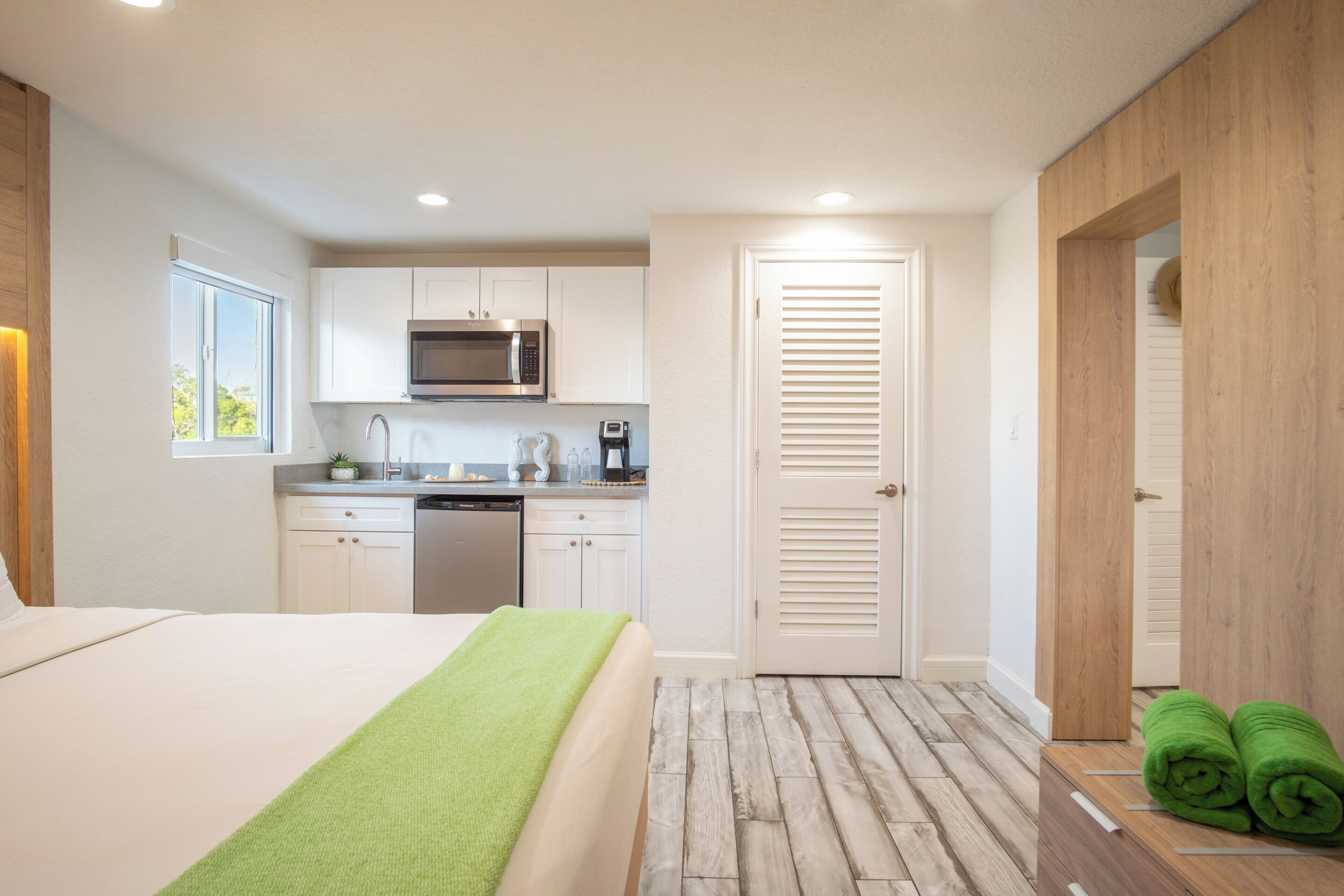 A modern hotel room with a bed, a small kitchenette, and a wooden floor.