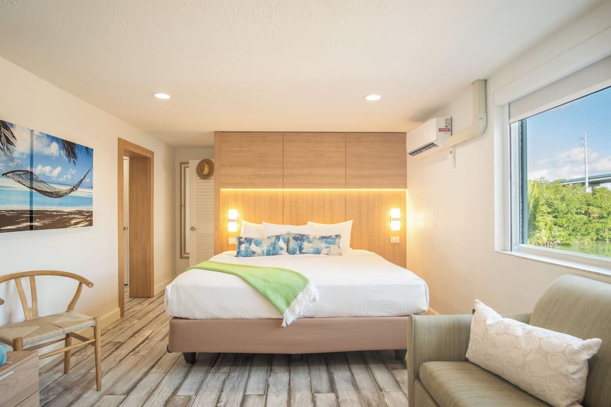 A modern hotel room with a large bed, wooden headboard, and a view of greenery through the window.