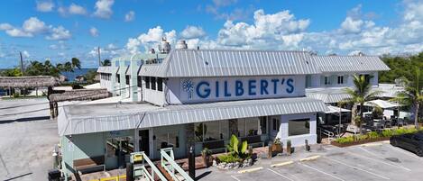 A building with a sign reading "GILBERT'S" and a covered outdoor seating area with plants.