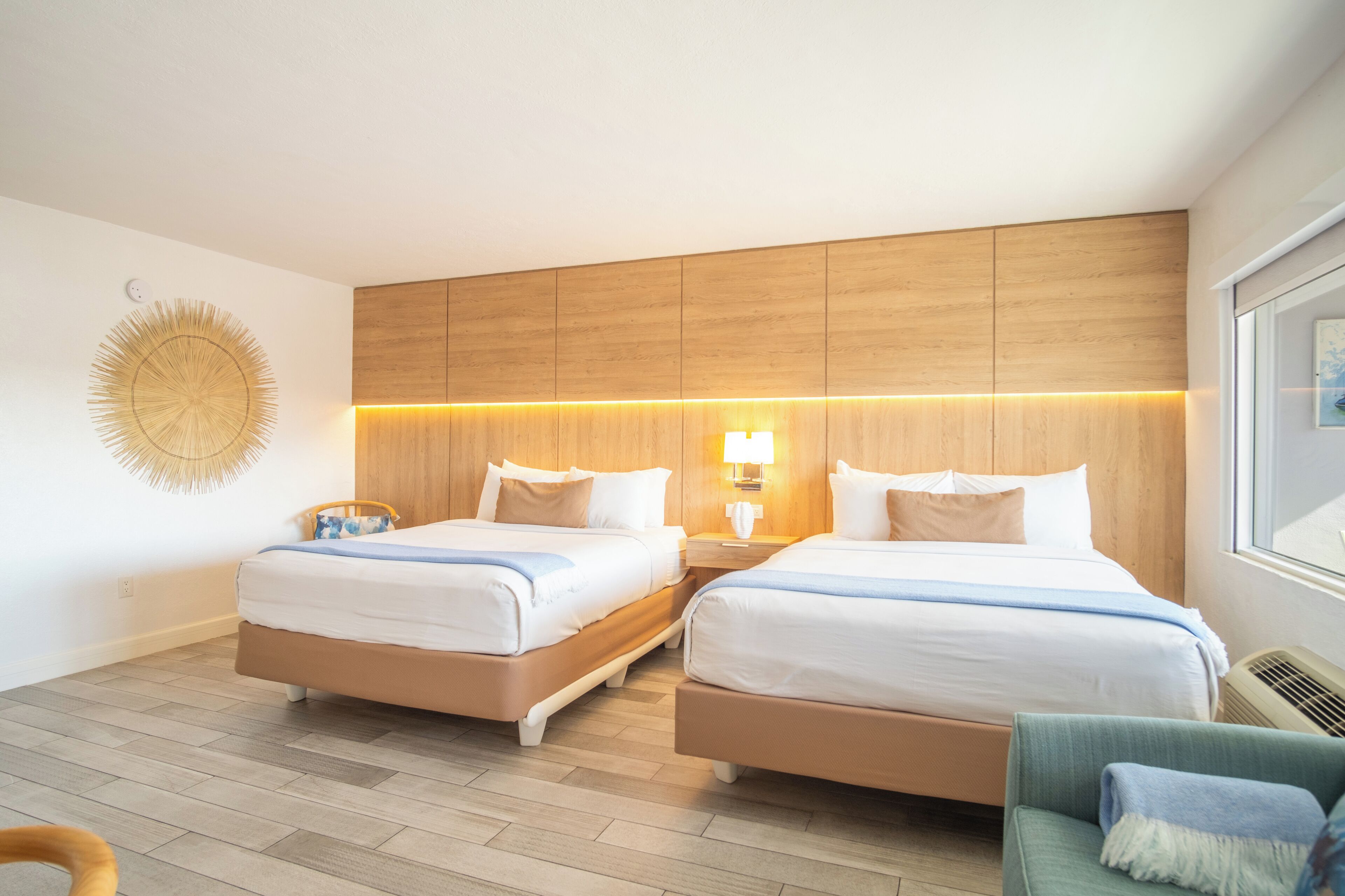 A hotel room with two beds, wooden headboard, bedside lamps, a wall decor, and a window.