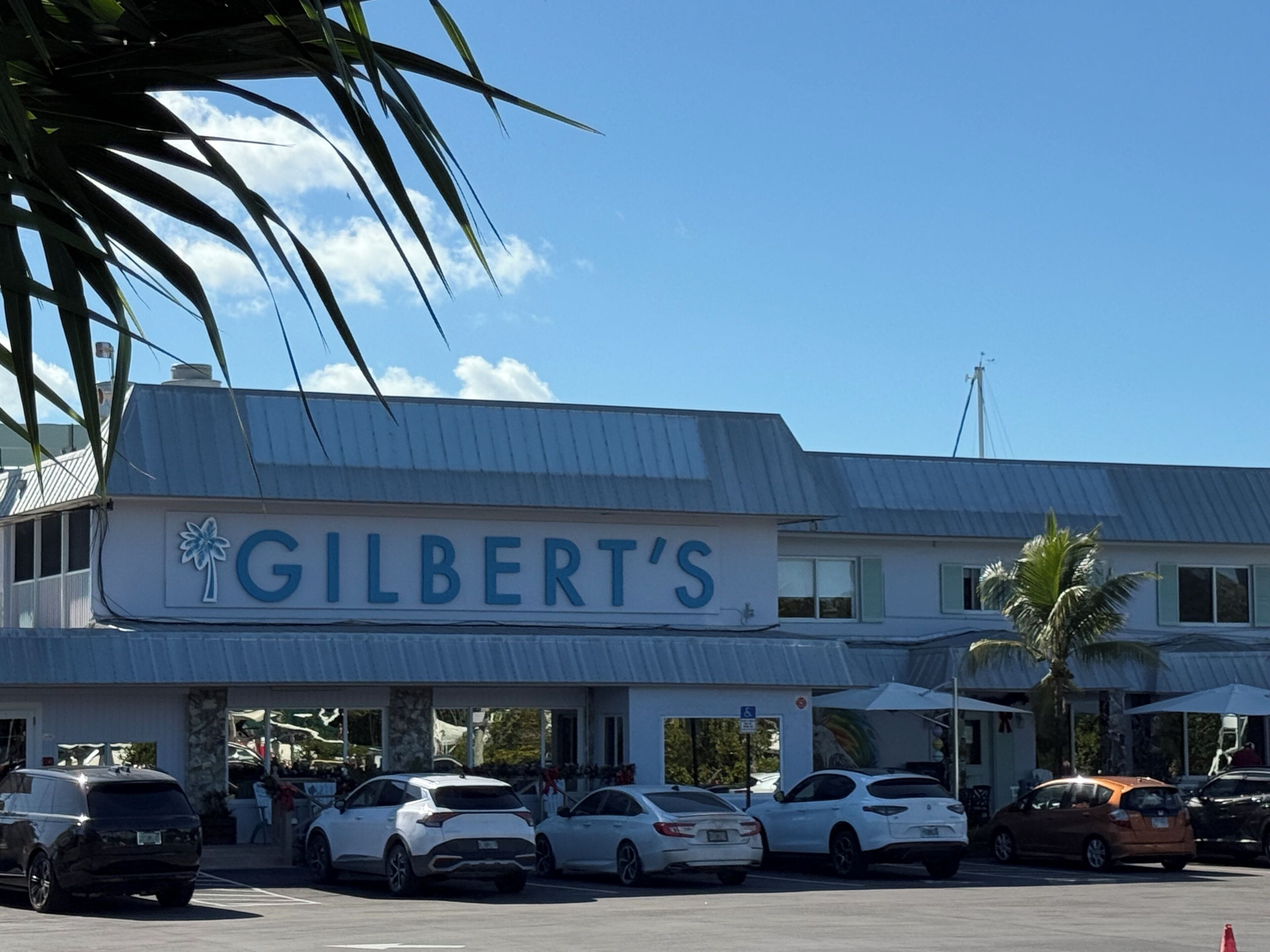 Un edificio con un cartel que dice "GILBERT'S" y un estacionamiento con varios coches.