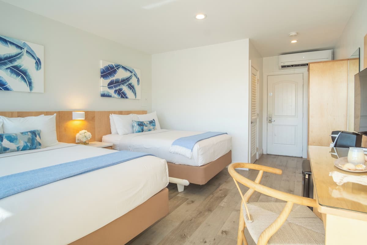 A hotel room with two beds, a desk with a chair, and a door leading to a bathroom.