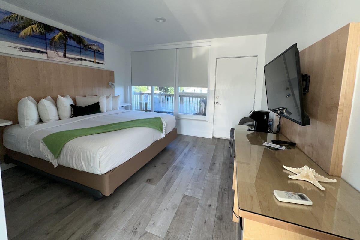 A modern hotel room with a large bed, a TV, and a balcony with a view.