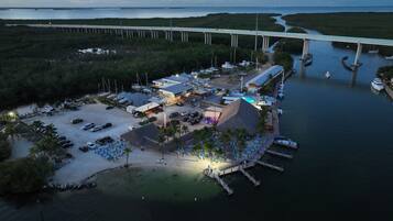 An aerial view of a coastal resort with a marina, a bridge in the background, and a large building with a pool.