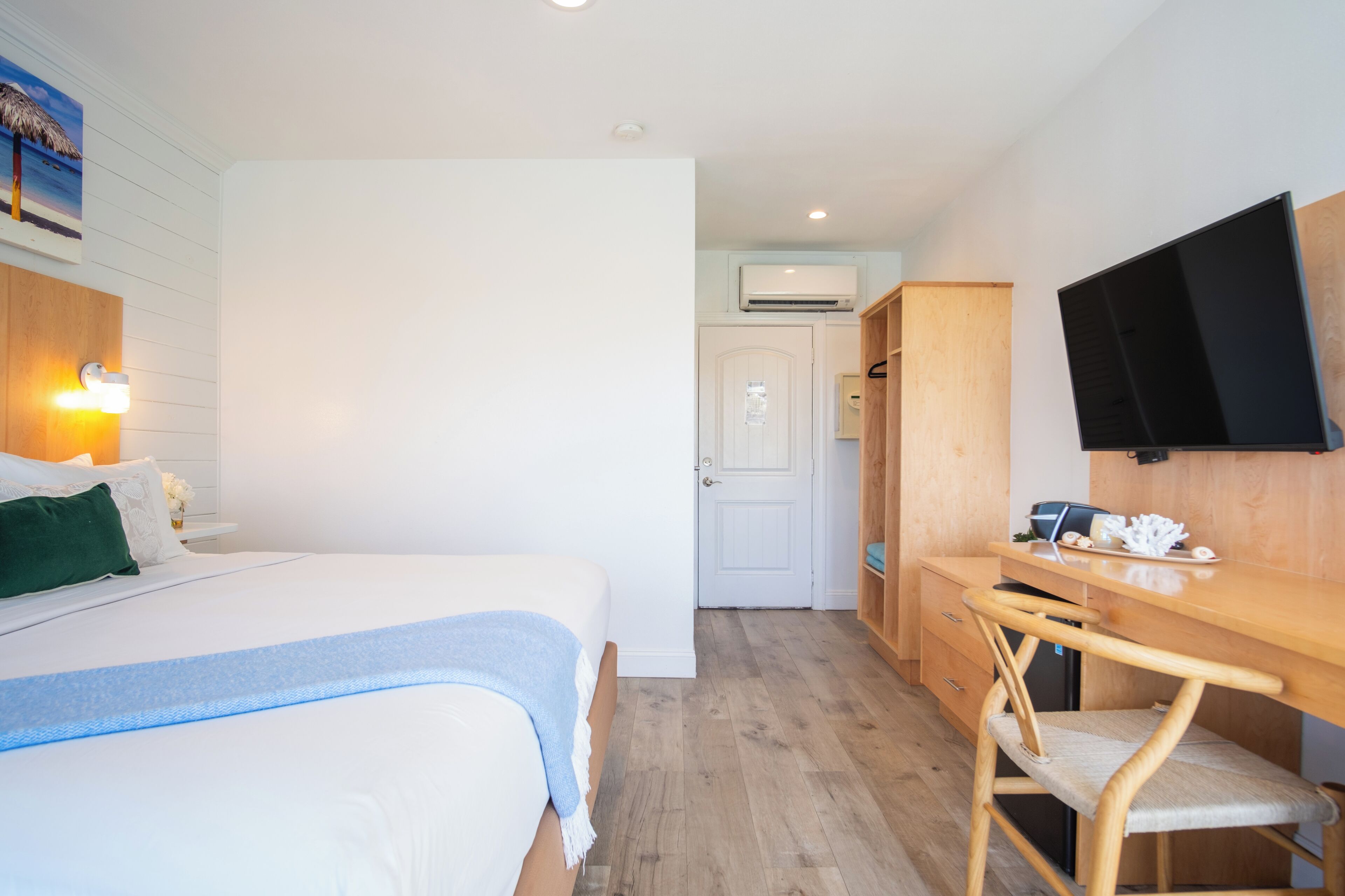 A hotel room with a bed, a desk, a chair, a TV, and a wardrobe.