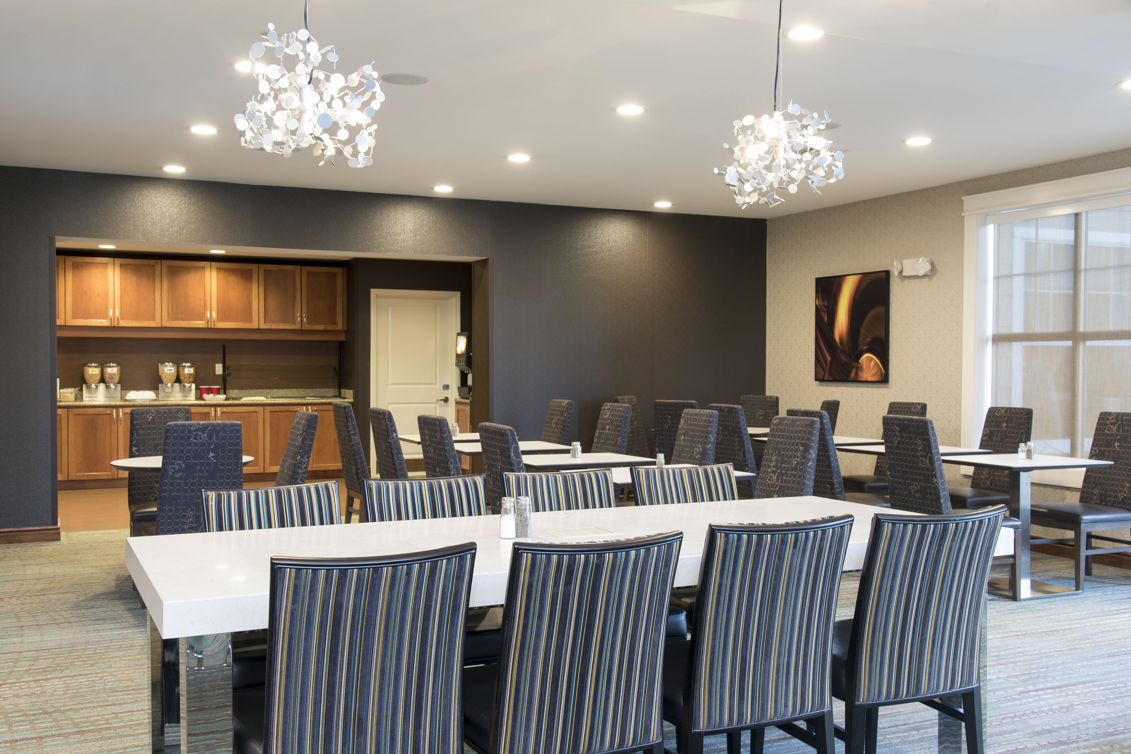 Une salle de conférence équipée de tables et de chaises, un coin cuisine et une grande fenêtre.