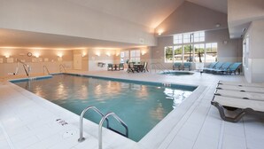 An indoor swimming pool with clear water, surrounded by lounge chairs and tables, and a view of the outside through large windows. - Residence Inn Marriott Moline (Moline)
