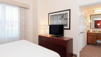 Una camera d'albergo con un letto, una televisione su un comò in legno, un quadro appeso al muro e un bagno visibile attraverso una porta aperta.