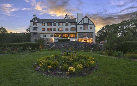 A large, multi-story building with a symmetrical facade, a stone foundation, and a well-maintained garden with a variety of flowers and shrubs.