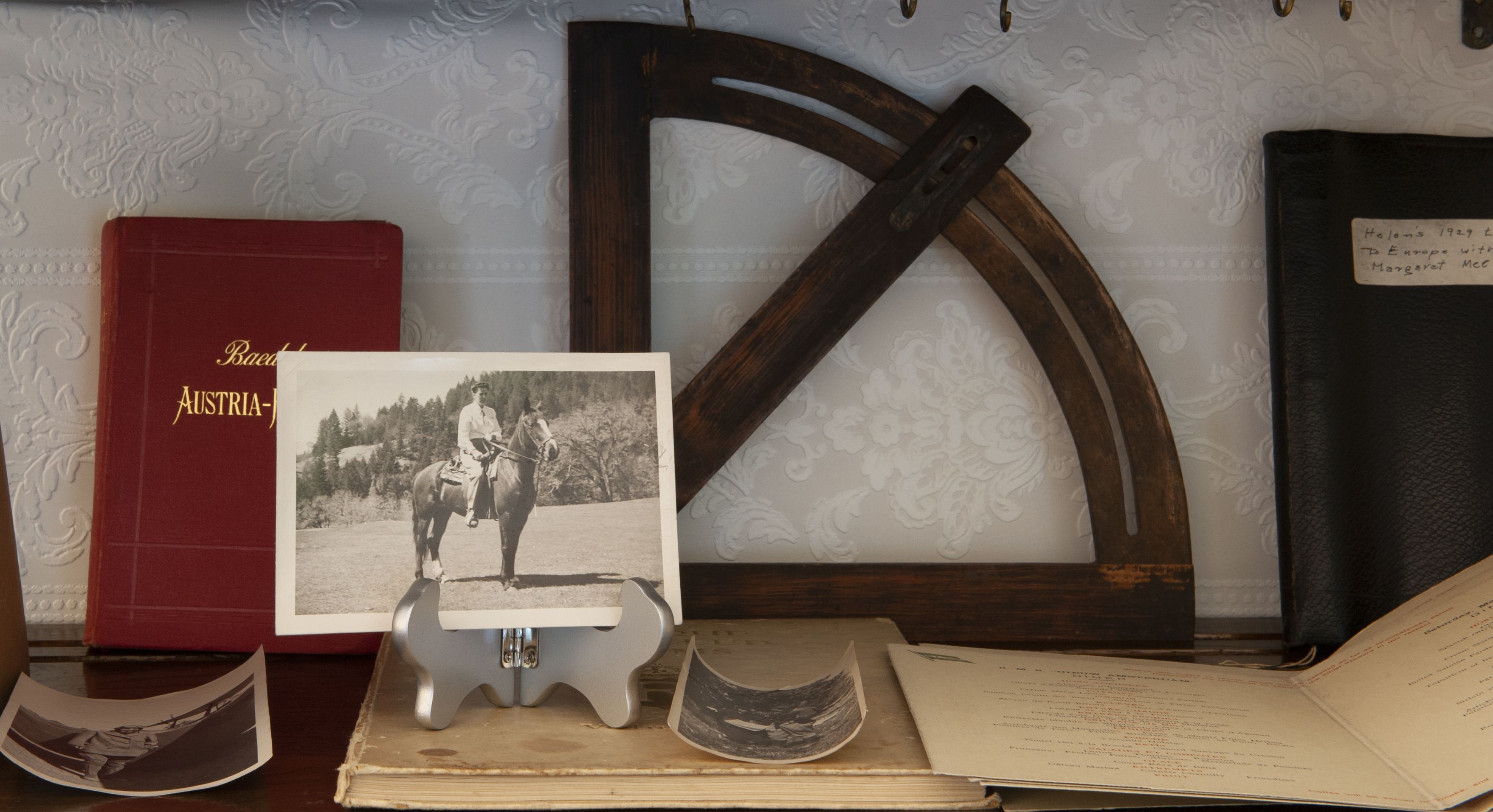 A desk with a red book titled 'Austria', a black and white photograph, a metal stand, and an open book with handwritten notes.
