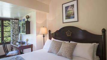 A neatly made bed with a dark headboard, a desk with a lamp, a globe, and a window with curtains.
