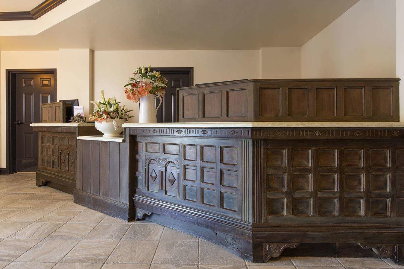 A dark wooden reception desk with a white countertop and a vase of flowers.