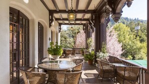 A covered patio with wicker furniture and a glass table, overlooking a garden with cherry blossoms.